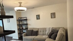 Una sala de estar con sofá, una mesita redonda, una estantería y un tapete decorativo.