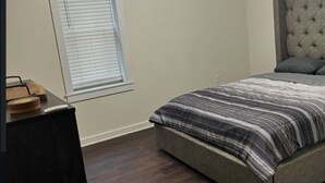 Un dormitorio con cama, ventana con persianas, mesita de noche y cabecero.