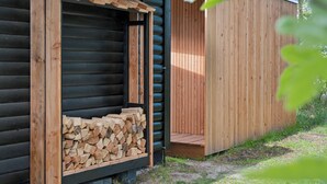 A log cabin with a wooden exterior, a window with a wooden frame, and a stack of firewood inside. - Cozy holiday home with wood-fired tub and sauna (Rødby)