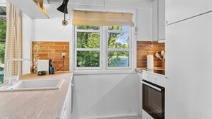 A kitchen with a window, white cabinets, a wooden countertop, a sink, a stove, and a brick backsplash. - Cozy holiday home with wood-fired tub and sauna (Rødby)