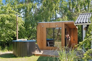 A wooden cabin with a large window, a deck, and a hot tub.