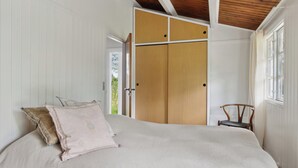 A bedroom with a bed, a wooden wardrobe, a chair, and a window. - Cozy holiday home with wood-fired tub and sauna (Rødby)