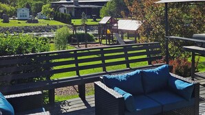 Un espace patio aménagé avec des meubles en osier, offrant une vue sur un terrain de jeux et des maisons en arrière-plan.