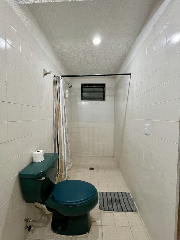 A small, tiled bathroom with a toilet, shower, and a window.