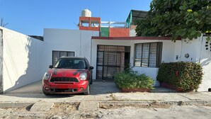 A red car parked in front of a white building with a small garden and a water tank on the roof. - Charming 2-bedroom house with Pool in gorgeous Puerto Escondido (Brisas de Zicatela)