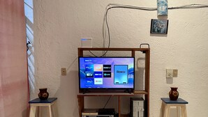 A television on a wooden stand with a Roku interface, surrounded by shelves with electronic devices and two small stools. - Charming 2-bedroom house with Pool in gorgeous Puerto Escondido (Brisas de Zicatela)
