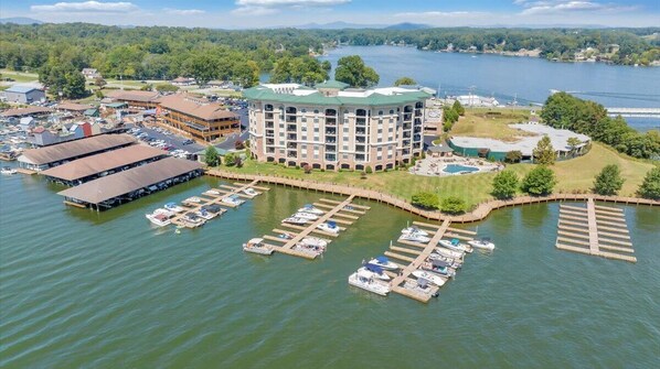 Un hotel frente al agua con varias construcciones, un puerto deportivo con barcos amarrados y un edificio grande con techo verde.
