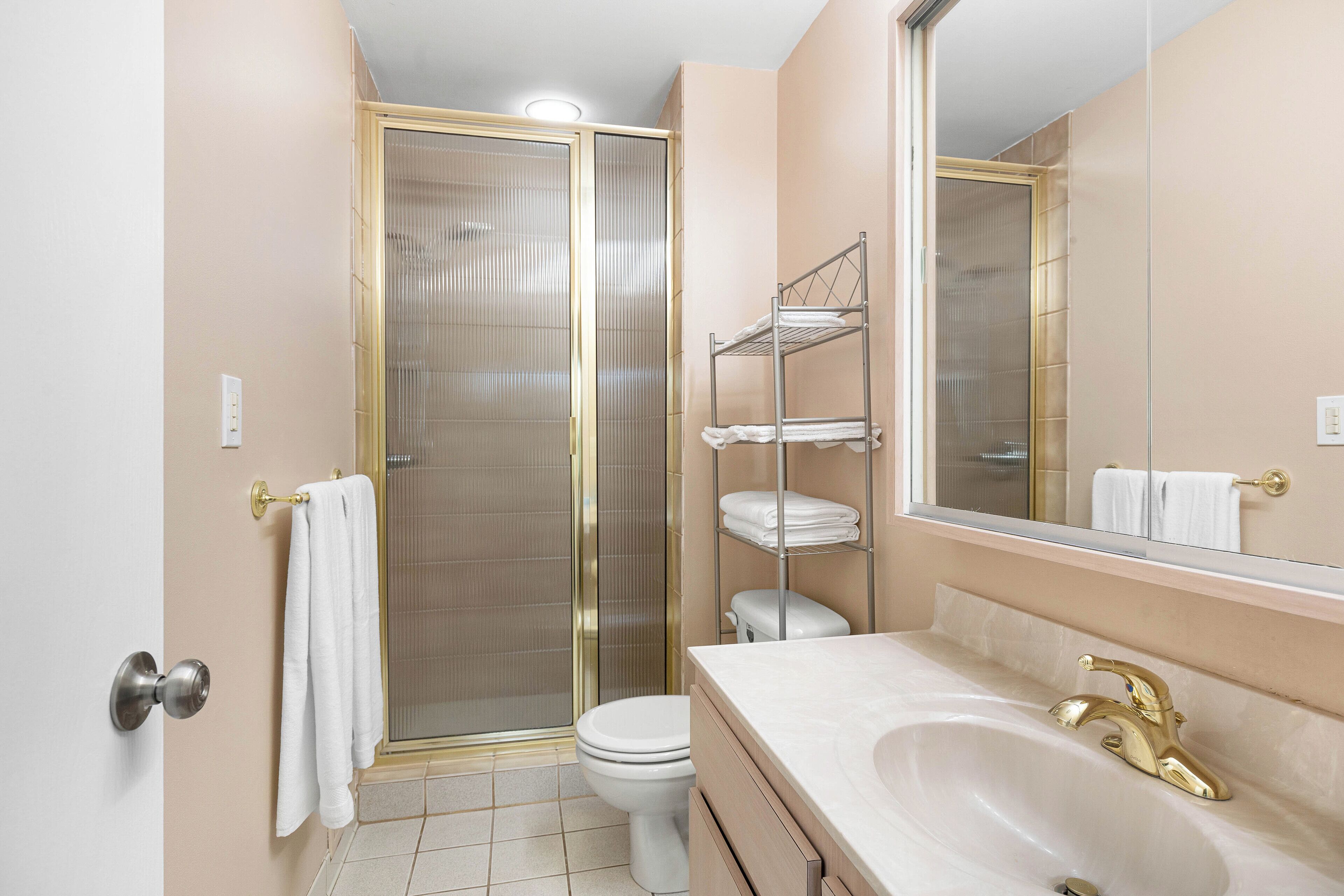 A bathroom with a shower, toilet, vanity, and a large mirror.