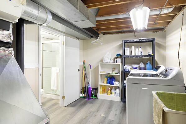 A laundry room with a washing machine, shelves with cleaning supplies, and a broom.