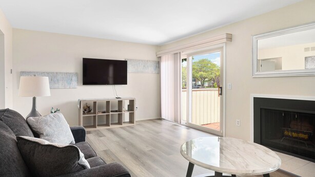 Ein Wohnzimmer mit einer Couch, einem Tisch, einem an der Wand montierten Fernseher, einem Kamin und einer Glastür zum Außenbereich.