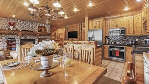 A rustic cabin interior with a stone fireplace, wooden dining table, and a kitchenette with modern appliances. - Abode at Black Bear #207, hot tub, pool & gym, Deer Valley (Park City)