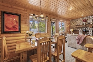 A wooden interior with a dining area, stone fireplace, and large windows.