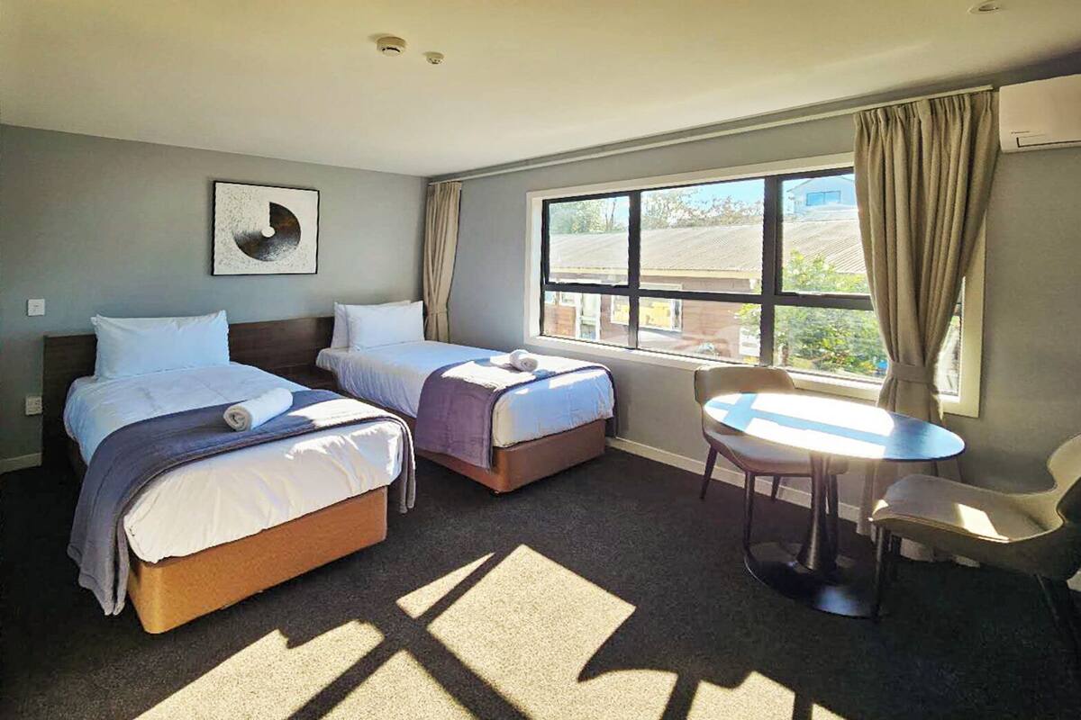 A hotel room with two beds, a small table, and a window with curtains.