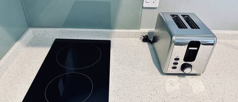 Une cuisine dotée d’une plaque de cuisson à induction noire et d’un grille-pain argenté, le tout posé sur un plan de travail à motifs.