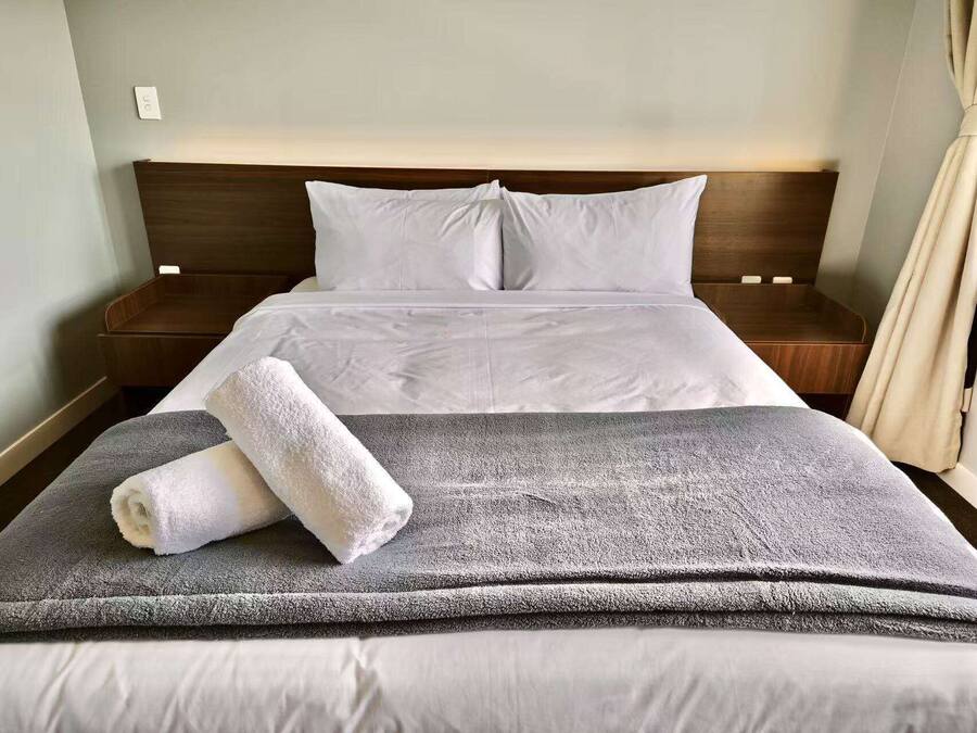 Una cama bien hecha con sábanas blancas, un edredón gris y una toalla blanca enrollada.
