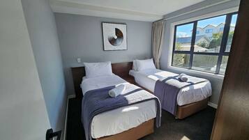 A hotel room with two single beds, a large window with a view of houses, and a ceiling light.
