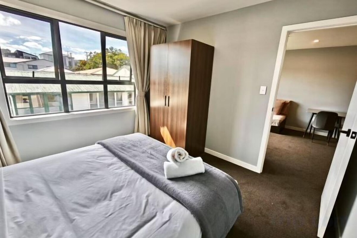 A hotel room with a bed, a wardrobe, a desk, and a view of the outside.