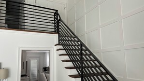 Una escalera con barandillas negras y escalones de madera que lleva a un rellano del segundo piso.