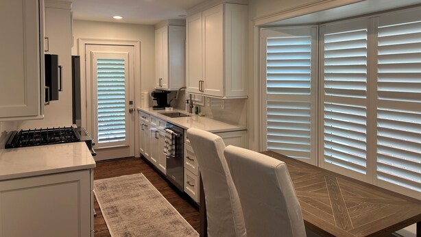 Una cocina moderna con armarios blancos, estufa integrada y un comedor con mesa y sillas de madera.