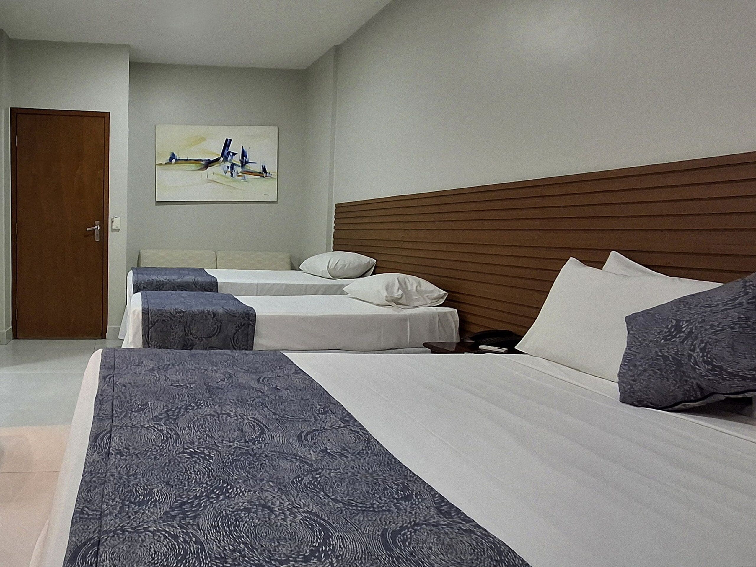 Quarto de hotel com duas camas, cabeceira de madeira e um quadro na parede.