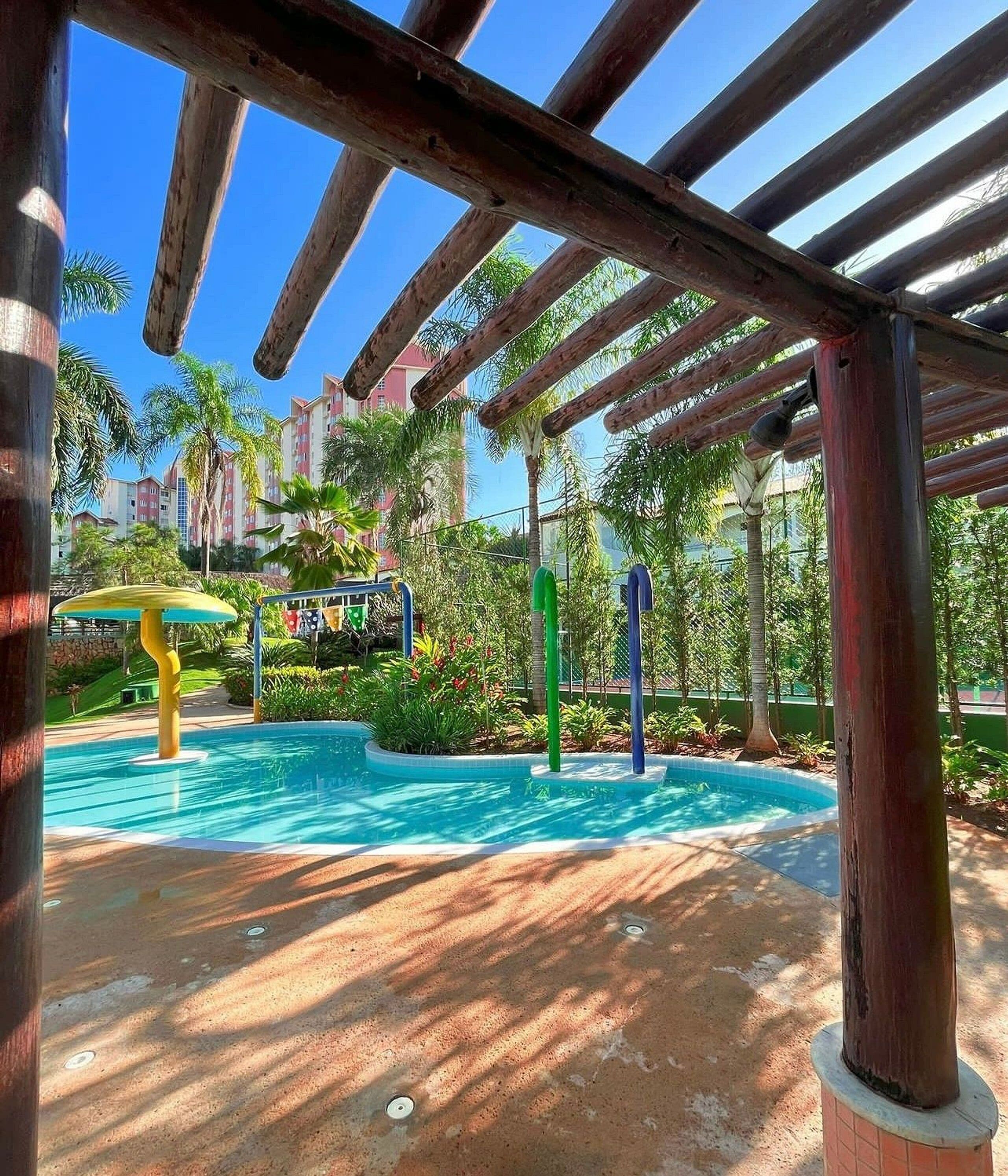 A covered outdoor area with a swimming pool, wooden pergola, and greenery.