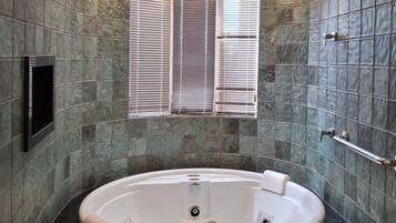 Une salle de bain moderne avec une baignoire sur pieds, une fenêtre avec stores et un téléviseur fixé au mur.