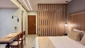 A hotel room with a wooden headboard, a bed with patterned bedding, a desk with a chair, a nightstand, and a wall-mounted lamp. - Hot Springs Hotel (Caldas Novas)
