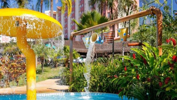 A swimming pool with a water feature, surrounded by palm trees and a building with a pink facade. - Hot Springs Hotel (Caldas Novas)