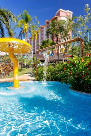 A swimming pool with a water feature, surrounded by palm trees and a building with a pink facade. - Hot Springs Hotel (Caldas Novas)
