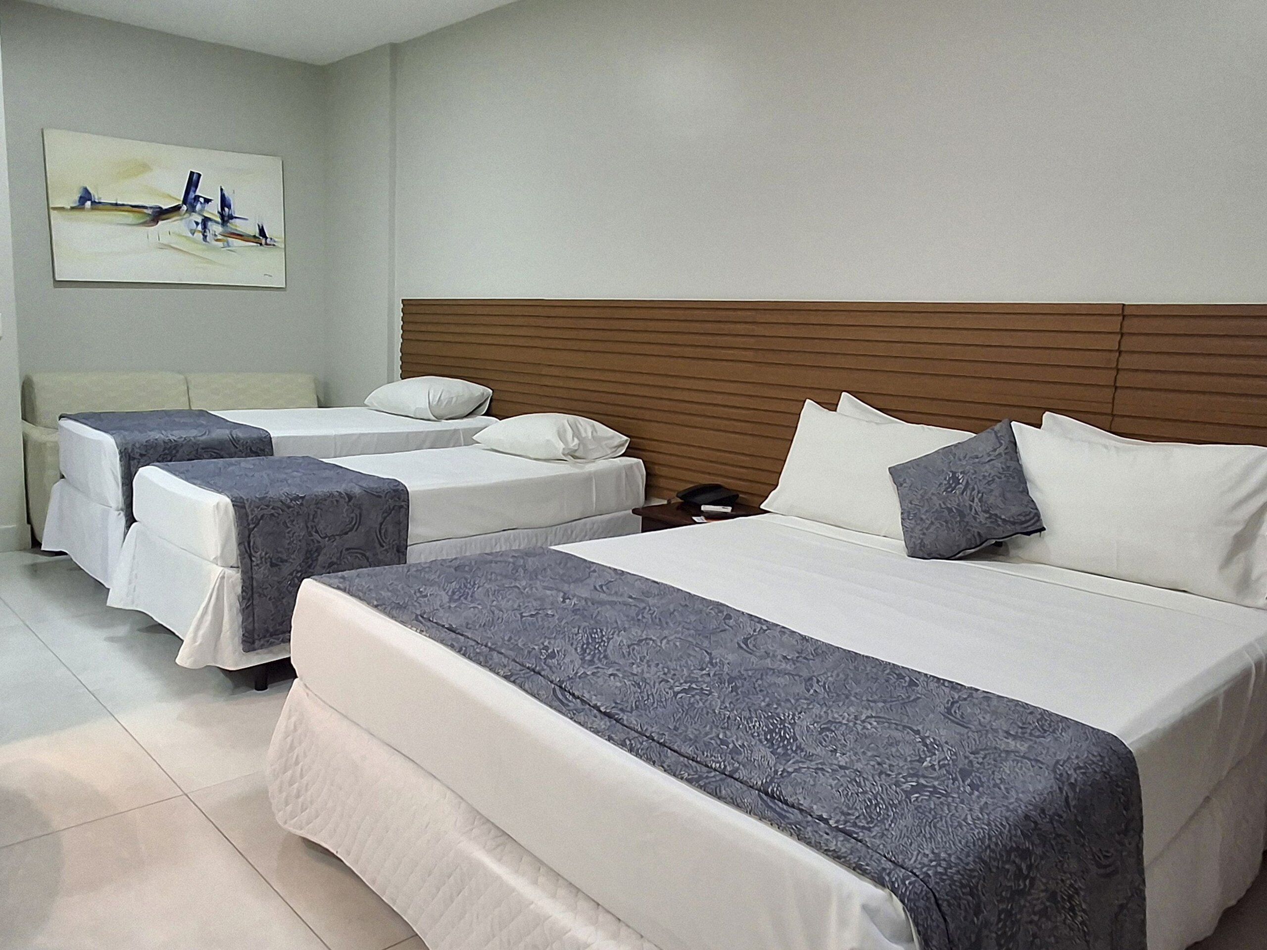 A hotel room with three beds, a wooden headboard, and a painting on the wall.