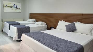 A hotel room with three beds, a wooden headboard, and a painting on the wall.
