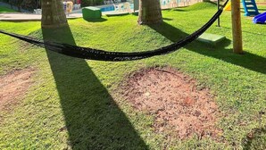 A park with a hammock, palm trees, a playground, and a building in the background. - Hot Springs Hotel (Caldas Novas)