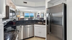 A modern kitchen with stainless steel appliances, a black granite countertop, and a view of the ocean.