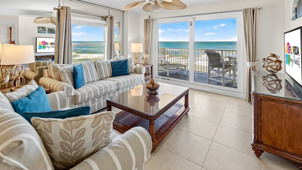 A spacious living room with a large sofa, a coffee table, and a view of the ocean through large sliding doors.