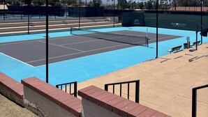 An outdoor tennis court with surrounding seating and a mountain backdrop.