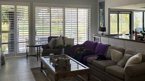 A spacious living room with a large window, a sofa, a coffee table, and a kitchen area with a counter and cabinets.