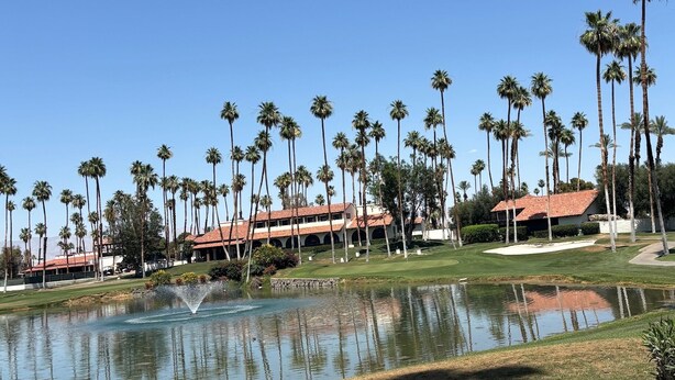 A golf course with a water feature, palm trees, and buildings with red-tiled roofs.