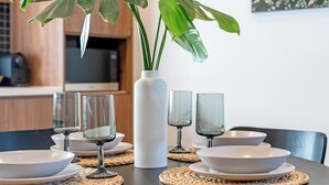 A dining table with white plates, glasses, and a white vase with green plants.