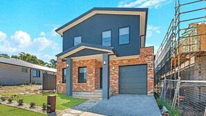 A modern two-story house with a brick facade, a front garage, and a well-maintained lawn.