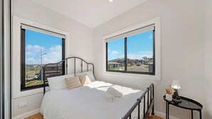 A bedroom with a bed, two windows, a bedside table, and a lamp.