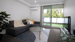 Uma sala de estar moderna com um sofá cinza, uma mesa de centro de vidro e uma grande porta de correr de vidro que dá para uma varanda.