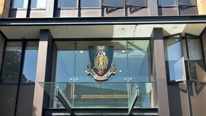 The entrance to St. John's College with a glass facade, a prominent crest above the doors, and a sign indicating the HINTZE BUILDING. - KozyGuru | Camperdown | Cozy 2-Bed Apt + Parking (Camperdown)