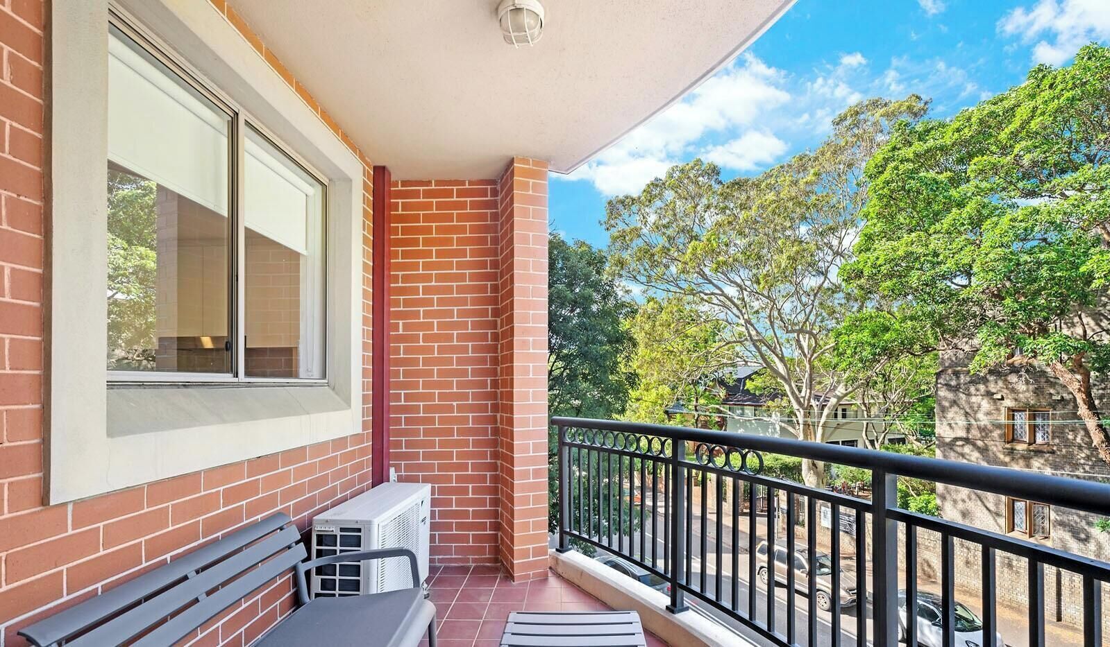 A balcony with a brick wall, a window, a bench, and a railing.