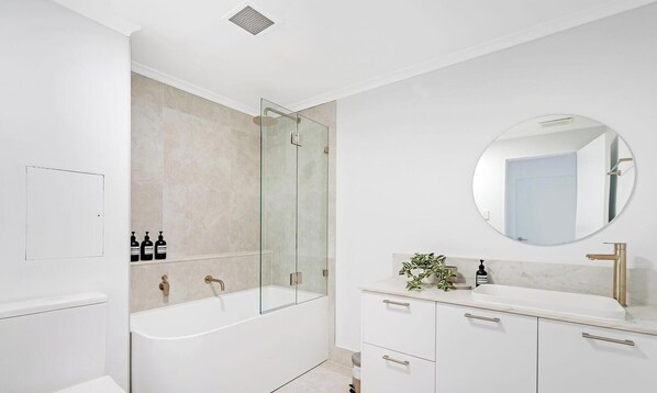 A modern bathroom with a glass-enclosed shower, a round mirror, and a white vanity with drawers. - KozyGuru | Camperdown | Cozy 2-Bed Apt + Parking (Camperdown)