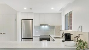A modern kitchen with white cabinetry, a stainless steel refrigerator, a built-in oven, and a sink. - KozyGuru | Camperdown | Cozy 2-Bed Apt + Parking (Camperdown)