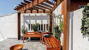 Een houten pergola met banken en potplanten in een binnenplaats.