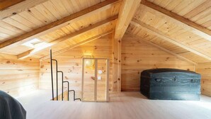 Een houten interieur met een schuine balkenkap, een wenteltrap, een wandlamp en een grote, donkere kist.