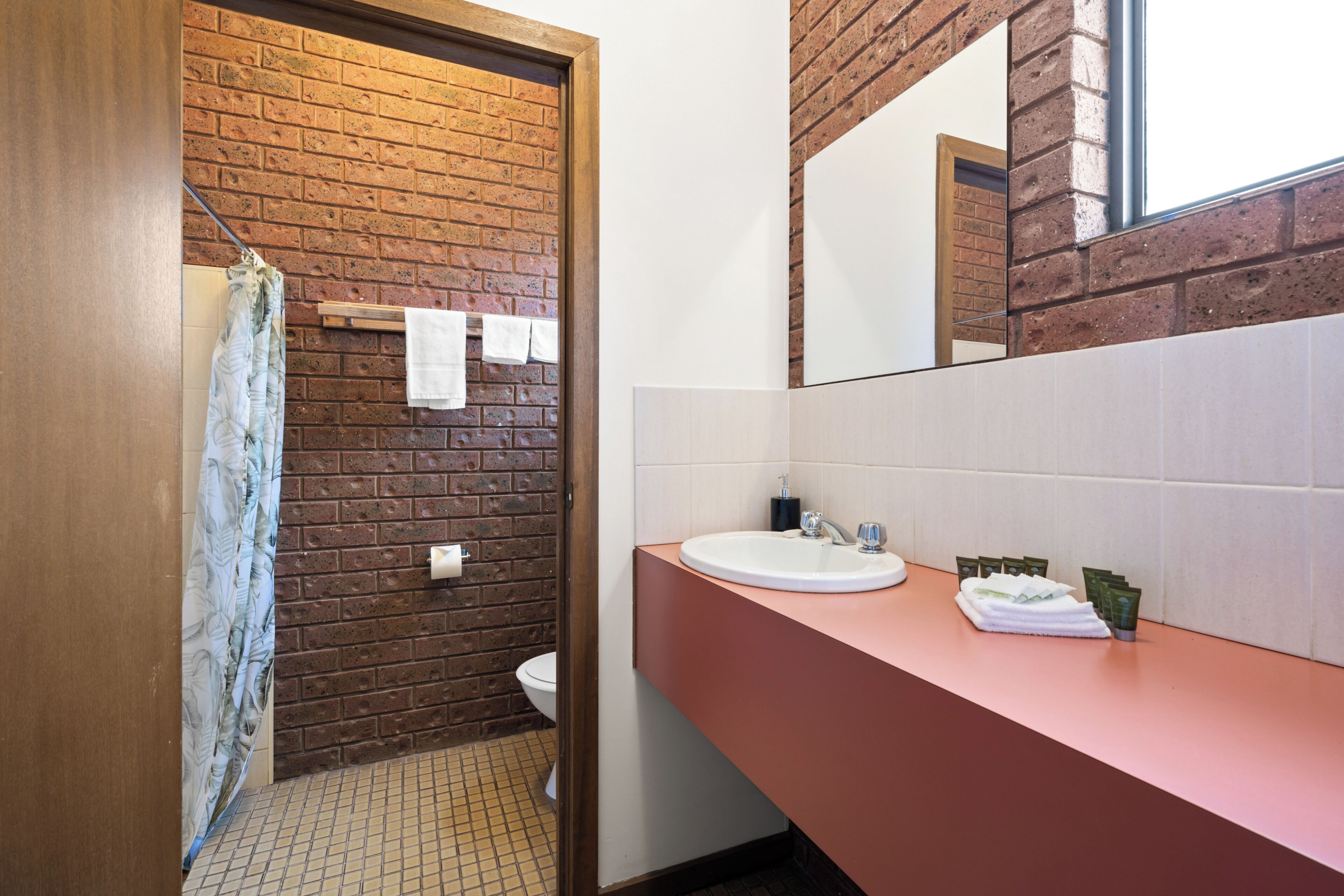 A bathroom with a brick wall, a white toilet, a sink with a mirror, and a shower curtain.