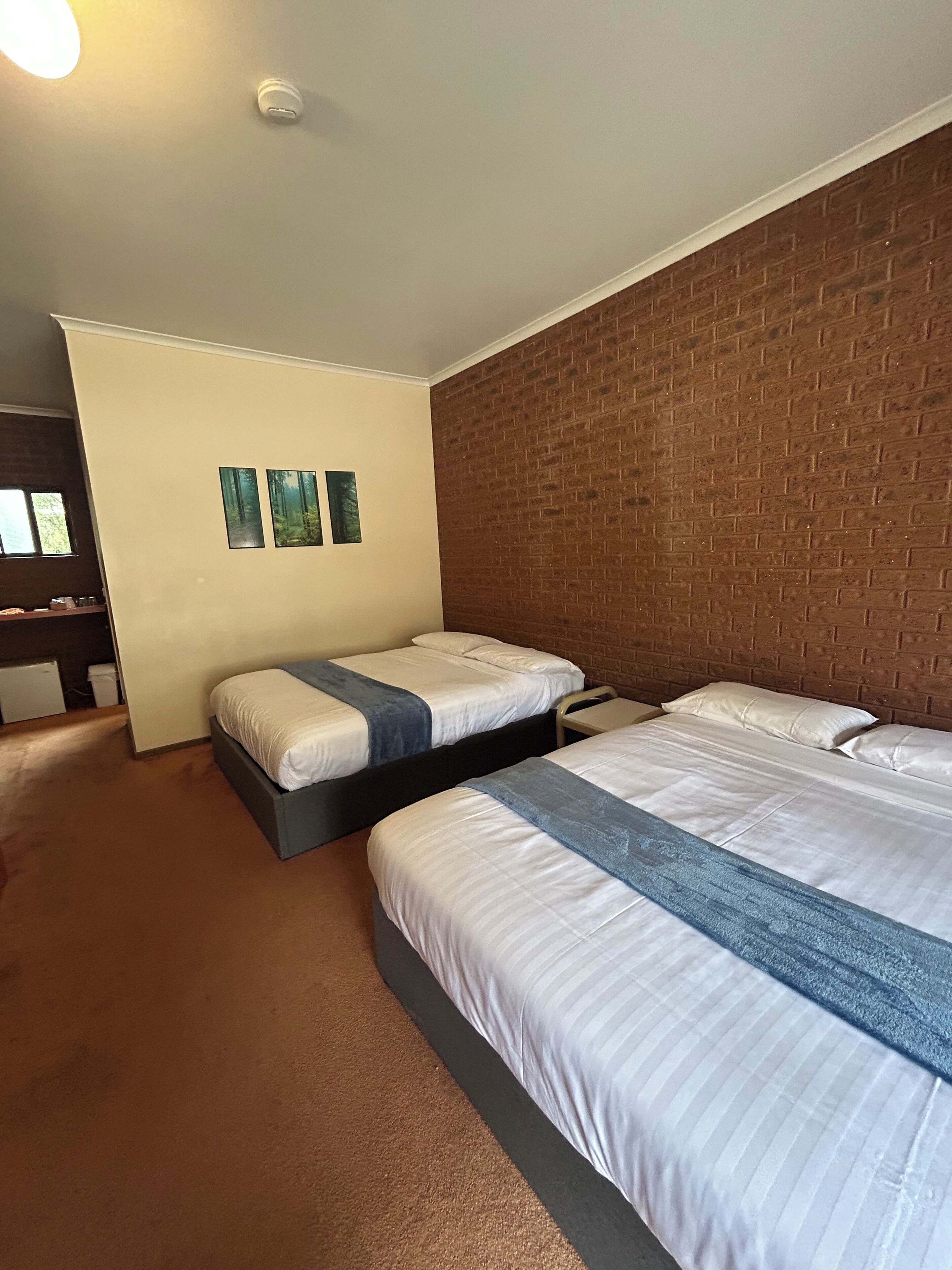 A hotel room with two beds, a brick accent wall, and a small window.