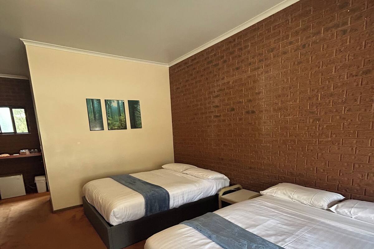 Habitación de hotel con dos camas, una pared decorativa de ladrillo y un ventanal.